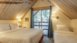 Une chambre mansardée chaleureuse, avec deux lits, une grande fenêtre et un plafond en bois.