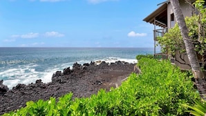A coastal view with a building adjacent to the ocean, featuring a balcony and lush greenery. - Pure Luxury! Chic Kitchen+Bath, Tile Floor, Sunset View Lanai, WiFi, Laundry Kanaloa 1902 (KAILUA-KONA)
