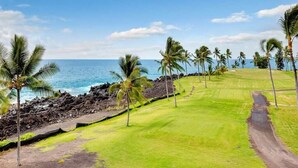 A golf course with a clear view of the ocean and palm trees. - Pure Luxury! Chic Kitchen+Bath, Tile Floor, Sunset View Lanai, WiFi, Laundry Kanaloa 1902 (KAILUA-KONA)