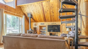 A cozy cabin interior with a large sofa, a fireplace, a television, and a spiral staircase. - Chalet #2, Charming Ski In/ Ski Out Steps to the M (Mammoth Lakes)