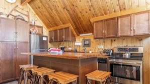 A kitchen with wooden cabinets, a central island with stools, a refrigerator, a stove, and a dishwasher. - Chalet #2, Charming Ski In/ Ski Out Steps to the M (Mammoth Lakes)