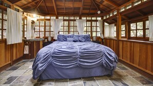 Une chambre située dans une cabane en bois, avec un grand lit, un sol en pierre et de nombreuses fenêtres.