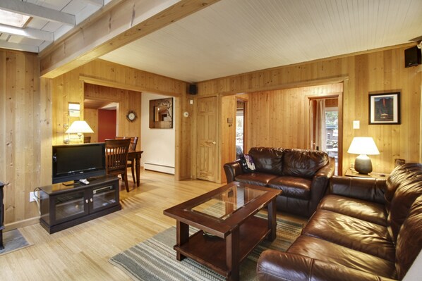 A spacious living room with wooden walls and floors, a leather sofa, a glass coffee table, and a television on a wooden stand. - Bird Watch From Private Spa, Teahouse, Wine Country, Dog Friendly! (Guerneville)