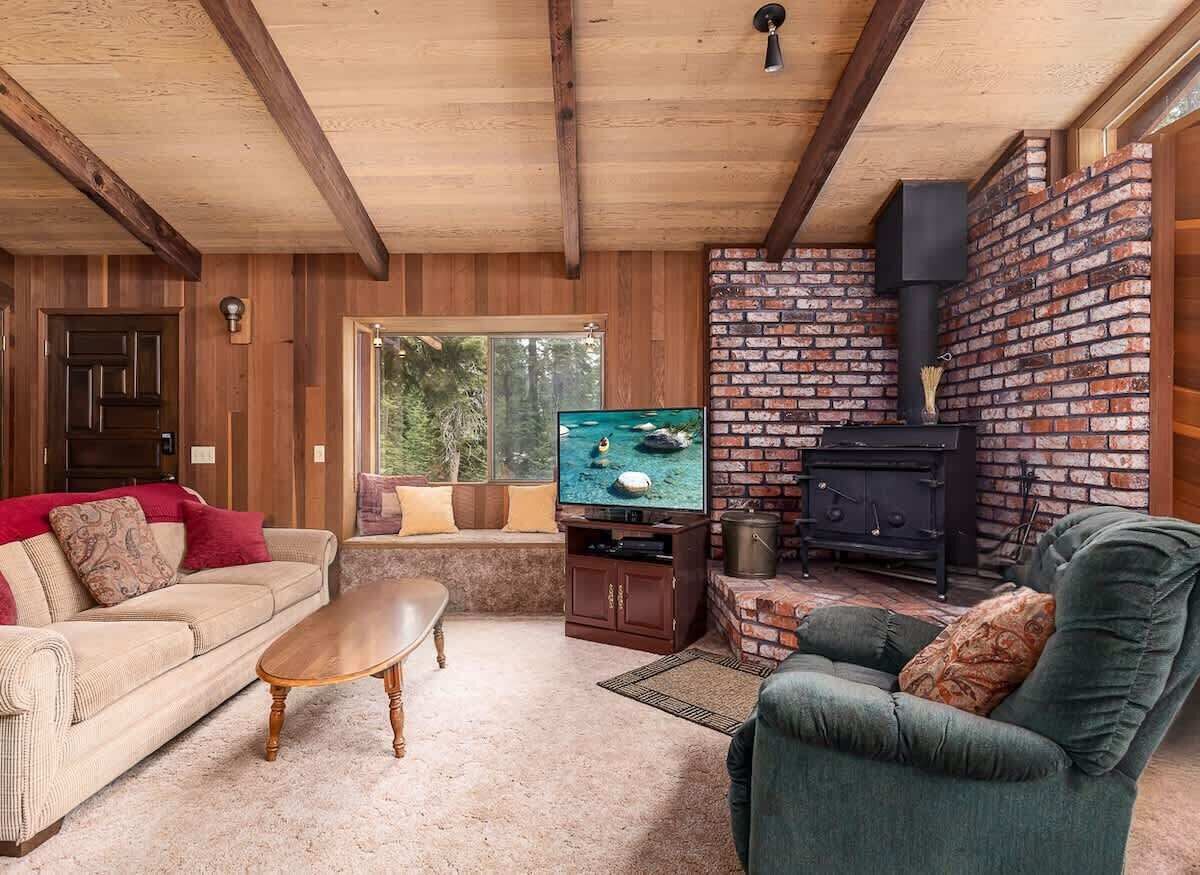 Un salon chaleureux avec un plafond en bois, une cheminée en briques, un téléviseur et un canapé.