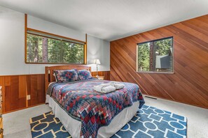 A bedroom with a wooden headboard, a plaid bedspread, and a blue patterned rug. - Villa Bossi Cabin Adjacent to Forest Land, Wood Stove, Full Kitchen, Deck Pets Welcome! (Carnelian Bay)