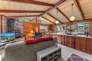 A cozy cabin interior with a fireplace, wooden walls, a dining area, and a bar. - Villa Bossi Cabin Adjacent to Forest Land, Wood Stove, Full Kitchen, Deck Pets Welcome! (Carnelian Bay)