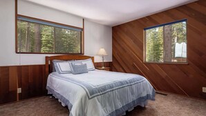 Une chambre à coucher avec un lit, deux fenêtres, une lampe et un lambris en bois.
