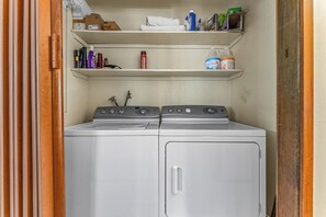 A laundry area with two front-loading washing machines, shelves above containing cleaning supplies, and a wooden door frame. - Villa Bossi Cabin Adjacent to Forest Land, Wood Stove, Full Kitchen, Deck Pets Welcome! (Carnelian Bay)
