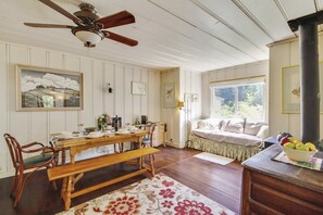 A cozy room with a wooden dining table, chairs, a bench, a bed with a window, and a ceiling fan.