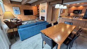 Un espacio de sala acogedor con pared de madera, televisor, chimenea y una mesa de comedor con sillas.