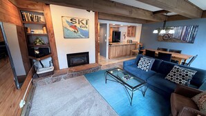 Una sala de estar acogedora con chimenea, un sofá, una mesa de centro y una cocina al fondo.
