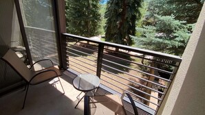Un balcón con una mesa y sillas, con vista a una zona boscosa.