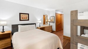 Ein Schlafzimmer mit einem Bett, Nachttischen, einer Kommode, einem Spiegel und einer Tür.