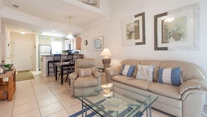 Amplia sala de estar con una mesa de centro de vidrio, sofá color beige y una zona de comedor con sillas y una mesa.