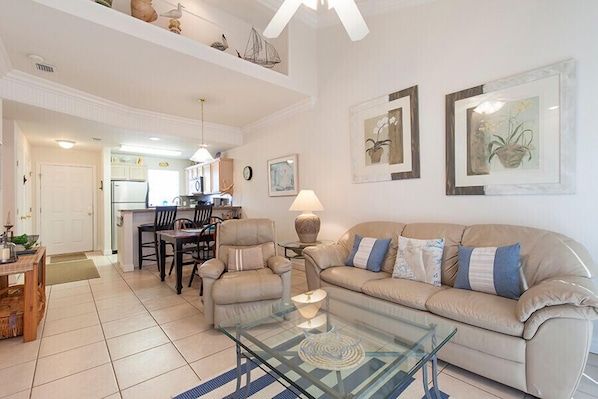 A spacious living room with a glass coffee table, beige sofa, and a dining area with chairs and a table.
