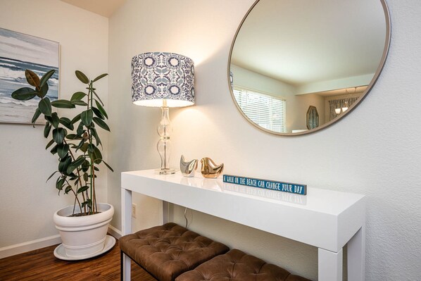 A white console table with a lamp, a mirror, a potted plant, and a sign.