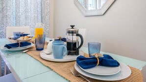 Uma mesa de café da manhã posta com pratos, xícaras e uma cafeteira, com um espelho na parede.