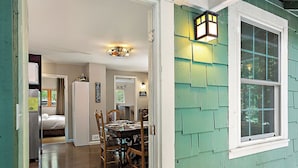 A dining area with a wooden table and chairs, a ceiling light fixture, and a window with a view of trees. - Monte Rio Treehouse ~ Dog Friendly, Redwoods, Walk to Restaurants and River (Monte Rio)