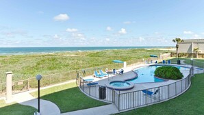 A pool area with a view of the ocean, surrounded by a fence and equipped with lounge chairs.