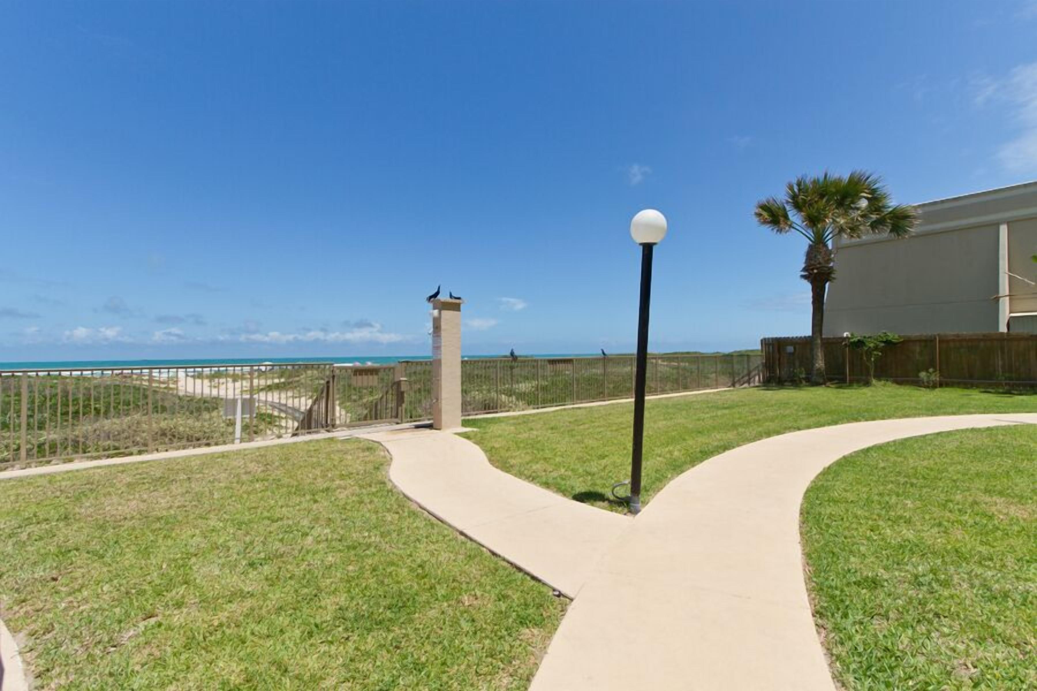 A pathway leading to a beach with a lamp post and a fence.
