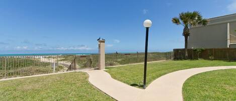 A pathway leading to a beach with a lamp post and a fence.