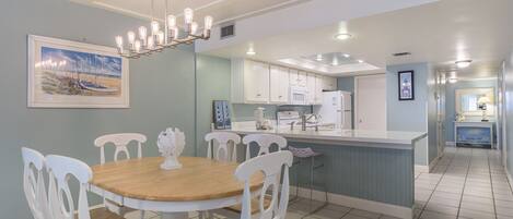 A dining area with a round wooden table and white chairs, a kitchen with white cabinets, and a hallway with a blue accent wall.