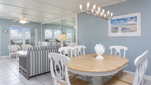 A dining area with a wooden table and white chairs, a striped sofa, and a ceiling fan.