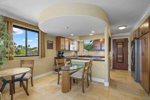A modern kitchen with a glass dining table, wooden chairs, and a view of the outdoors.