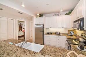 A kitchen with white cabinets, a stainless steel refrigerator, a microwave, and granite countertops.