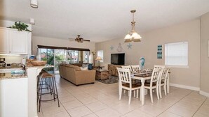 Uma sala de estar ampla com mesa de jantar, sofá e cozinha com um banco.