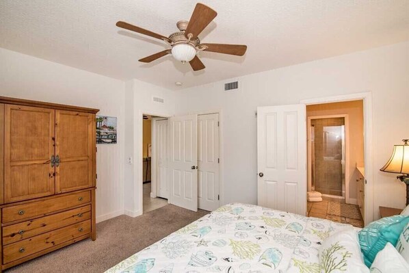 A bedroom with a bed, a wooden wardrobe, a ceiling fan, and a door leading to a bathroom.