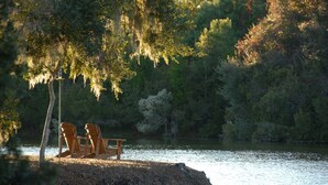 A lakeside setting with two wooden Adirondack chairs under a tree with hanging moss. - Classic Second Row Beach House, Short Walk to the Beach (Georgetown)