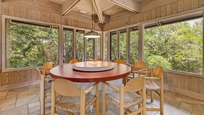 A wooden dining room with a round table and chairs, large windows, and a hanging light fixture. - Classic Second Row Beach House, Short Walk to the Beach (Georgetown)