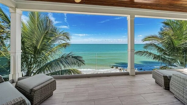 A covered outdoor area with a view of the ocean, wicker furniture, and a ceiling fan. - Felicity: Luxury Bayfront Home, Heated Pool, Hot tub and more! (Anna Maria)