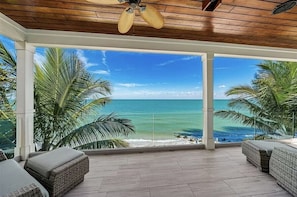 A covered outdoor area with a view of the ocean, wicker furniture, and a ceiling fan. - Felicity: Luxury Bayfront Home, Heated Pool, Hot tub and more! (Anna Maria)