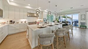 A modern kitchen with white cabinetry, a large island, and pendant lighting. - Felicity: Luxury Bayfront Home, Heated Pool, Hot tub and more! (Anna Maria)
