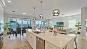 A modern kitchen with a large island, pendant lights, and a view of the ocean. - Felicity: Luxury Bayfront Home, Heated Pool, Hot tub and more! (Anna Maria)