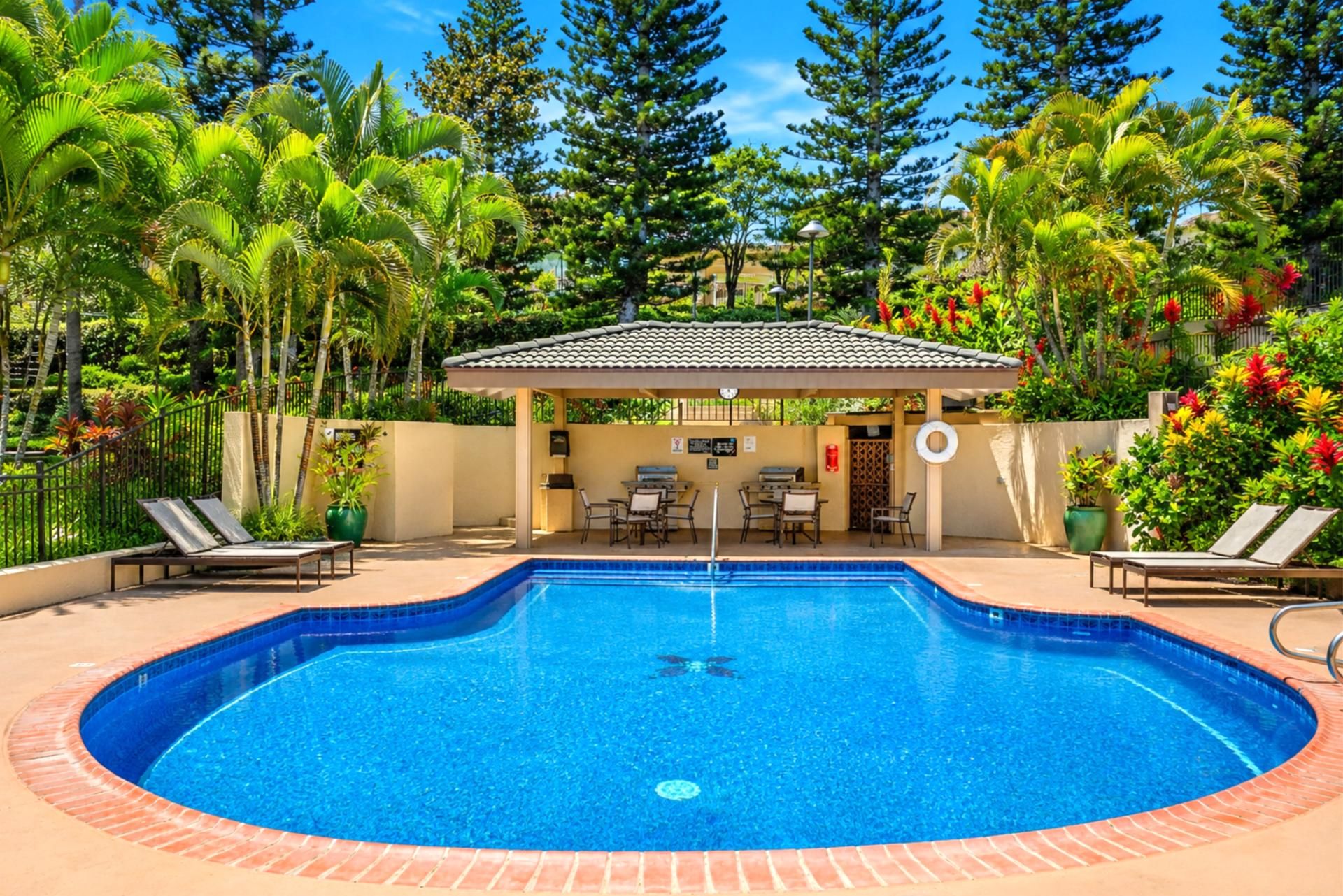 Una piscina circular con borde de azulejos, rodeada de sillas de descanso y una zona de estar cubierta.