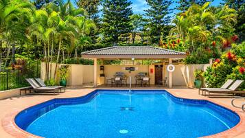 Una piscina circular con borde de azulejos, rodeada de sillas de descanso y una zona de estar cubierta.