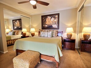 A well-lit bedroom with a large bed, two bedside tables with lamps, a wooden bench, and a ceiling fan.