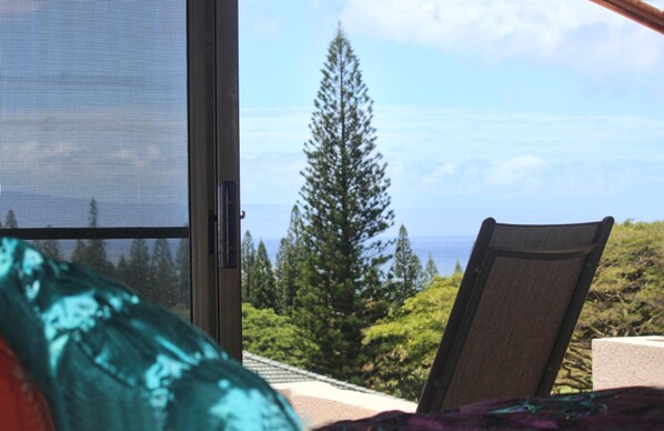 A room with a large window, a chair, and a view of a forest and mountains.