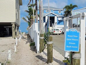 Un panneau indiquant un accès privé à la plage, une clôture en bois et un bâtiment à la façade bleue.