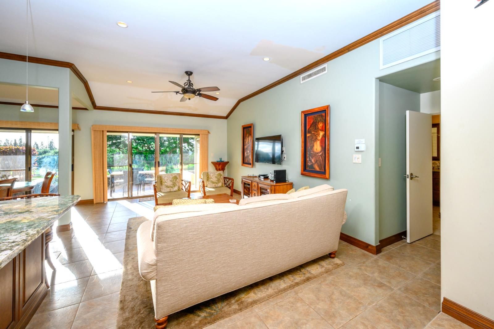 A spacious living room with a large sofa, a dining area with a table and chairs, a kitchen area with a countertop, and a ceiling fan.