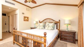 A bedroom with a wooden bed, two bedside tables with lamps, a ceiling fan, and a door leading to another room.