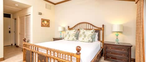 Une chambre à coucher avec un lit en bois, deux tables de chevet avec des lampes, un ventilateur de plafond et une porte donnant sur une autre pièce.