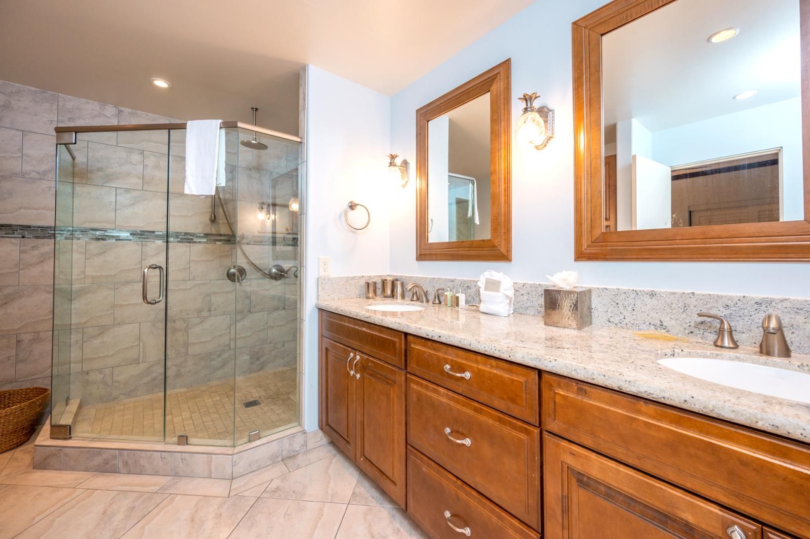 Un bagno moderno con doccia vetrata, mobile bagno in legno e due specchi.