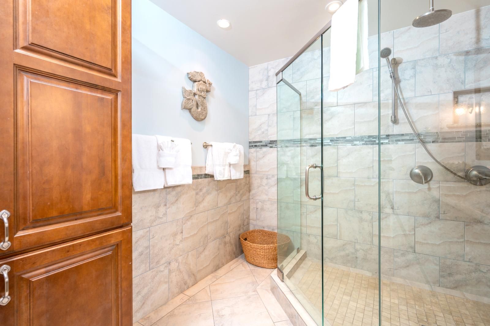 A bathroom with a glass shower enclosure, marble tiles, and wooden cabinets.