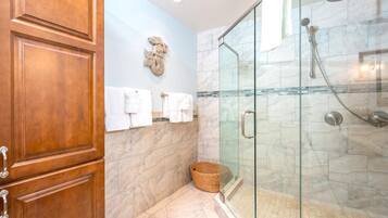 A bathroom with a glass shower enclosure, marble tiles, and wooden cabinets.