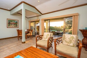 A spacious living area with a dining table, two wicker chairs, a wooden coffee table, and a large sliding glass door leading to an outdoor patio.