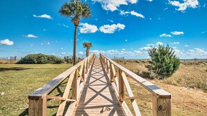 A wooden boardwalk leading through a grassy area with palm trees and a clear blue sky. - Just beyond the dunes Water's Edge is a cozy ocean view villa (Georgetown)
